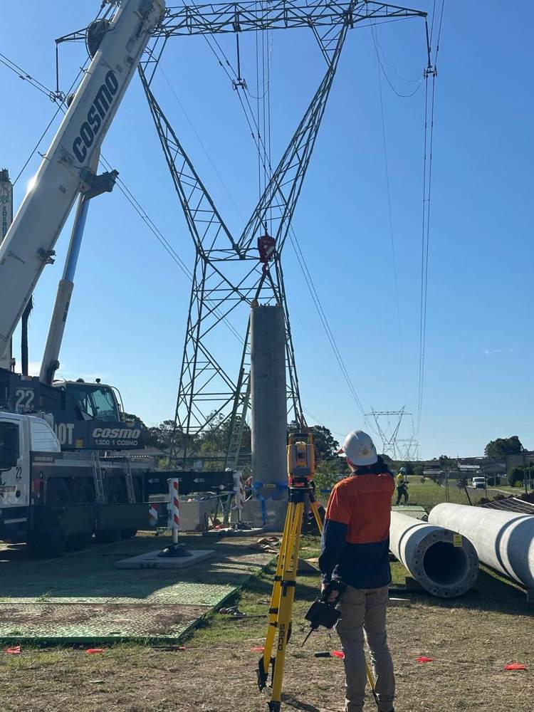 Crane placing a pole beside a transmission tower